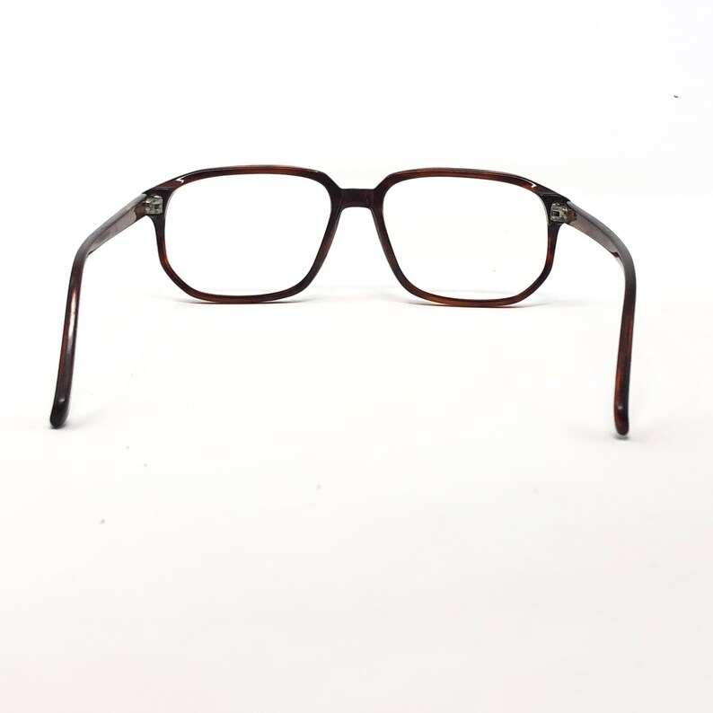 May include: Brown rectangular eyeglasses with clear lenses. The glasses have a classic, retro design with a dark brown frame and temples. The arms of the glasses are extended, showcasing the full shape and style of the eyewear.