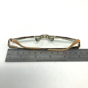 Peut inclure: Une paire de lunettes de lecture dor&eacute;es avec une monture en plastique marron et des verres transparents. Les lunettes sont mesur&eacute;es sur une r&egrave;gle, montrant une longueur de 10 centim&egrave;tres.