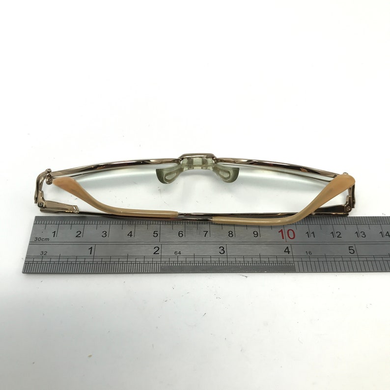 Peut inclure: Une paire de lunettes de lecture dor&eacute;es avec une monture en plastique marron et des verres transparents. Les lunettes sont mesur&eacute;es sur une r&egrave;gle, montrant une longueur de 10 centim&egrave;tres.