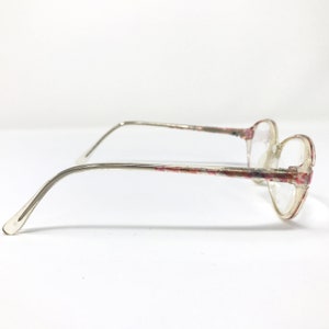 May include: Clear-framed eyeglasses with a floral pattern in pink and red. The glasses have a rounded shape and thin, silver-toned arms. The lenses are clear, and the overall design is vintage-inspired.