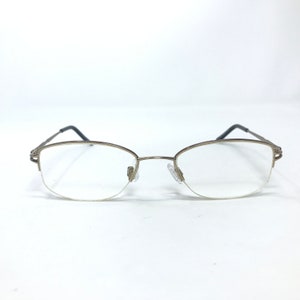 May include: A pair of gold-toned metal eyeglasses with clear lenses. The glasses have a rimless design and a subtle oval shape.