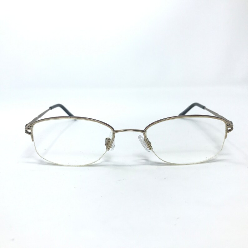 May include: A pair of gold-toned metal eyeglasses with clear lenses. The glasses have a rimless design and a subtle oval shape.