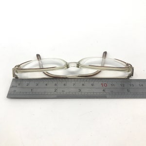 K&ouml;nnte beinhalten: Eine Brille mit transparentem Rahmen und braunen Akzenten, etwa 14 cm lang. Ein Metalllineal liegt neben der Brille auf einer wei&szlig;en Oberfl&auml;che.