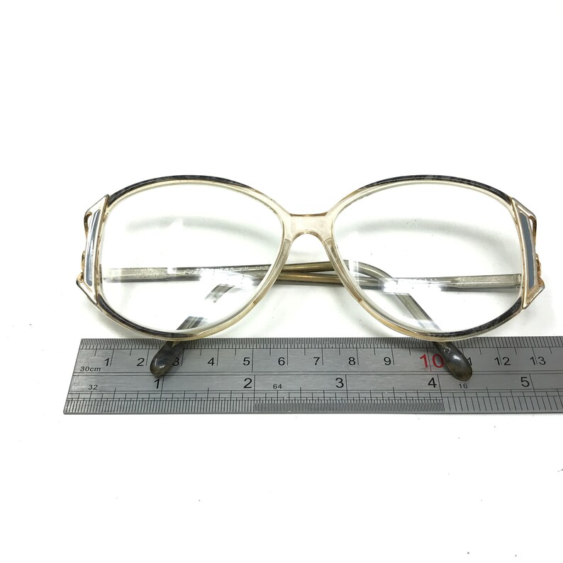 Puede incluir: Gafas ovaladas de pl&aacute;stico transparente con un borde marr&oacute;n alrededor de las lentes. Las gafas se miden con una regla, mostrando que el ancho de las lentes es de aproximadamente 10 cent&iacute;metros.