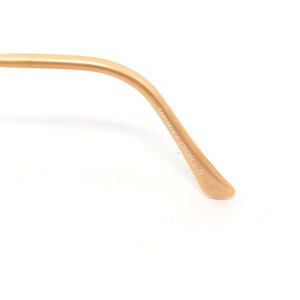 May include: Close-up of a gold-colored eyeglass arm. The text "Specsavers 1701004 L CE L71" is printed on the arm. The arm curves gently and ends in a rounded tip. The background is white.