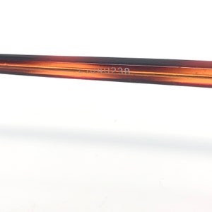 May include: Close-up of a portion of eyeglasses frame. The frame is a gradient of brown and amber. The text "51044238" is printed on the frame. The background is white.