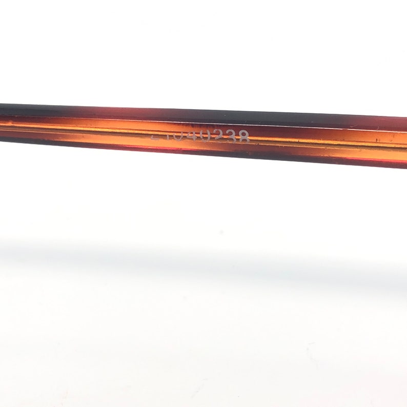 May include: Close-up of a portion of eyeglasses frame. The frame is a gradient of brown and amber. The text "51044238" is printed on the frame. The background is white.