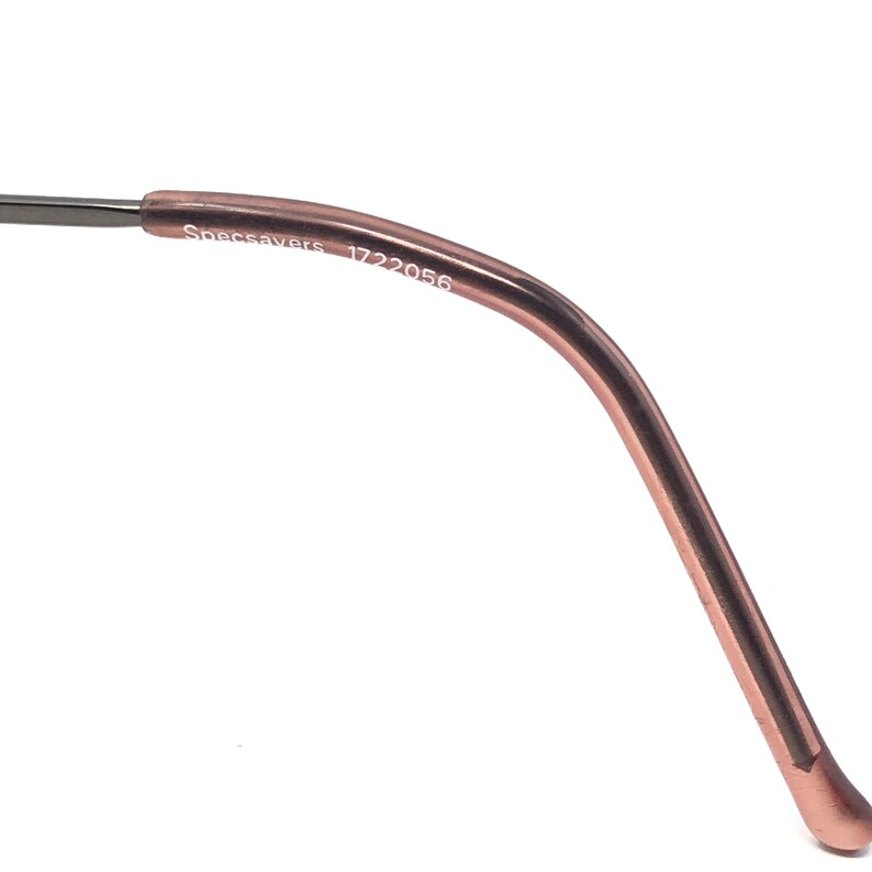 Puede incluir: Primer plano de una patilla de gafas de color oro rosa. El texto "Specsavers 1722056" est&aacute; impreso en la patilla. La patilla se curva hacia abajo y termina en una punta redondeada. El fondo es blanco.