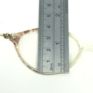 May include: A clear plastic frame with a brown and white pattern. The frame is measured with a ruler, showing a width of approximately 1.5 inches.