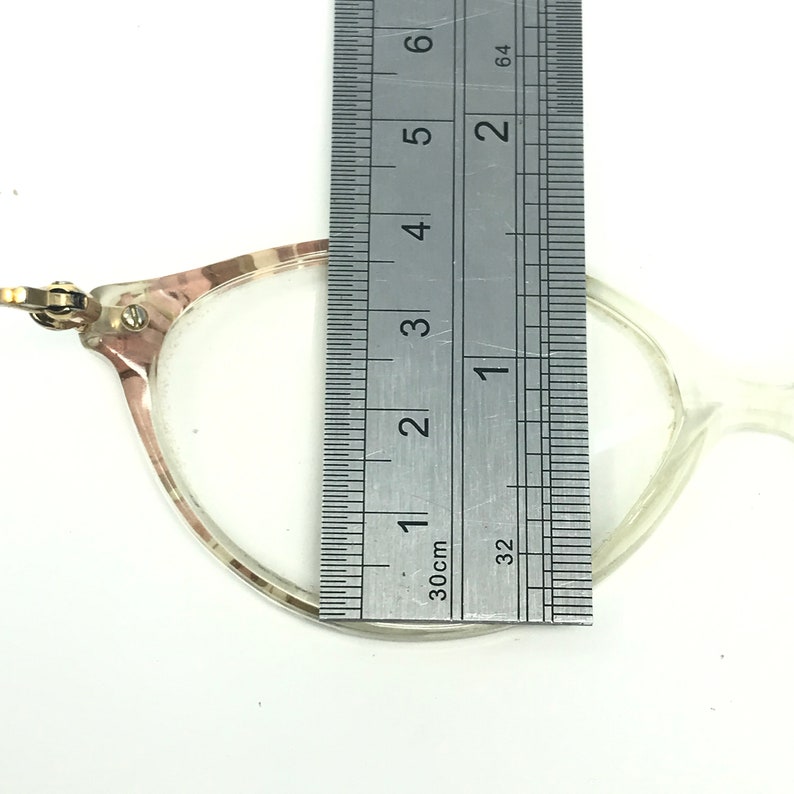 May include: A clear plastic frame with a brown and white pattern. The frame is measured with a ruler, showing a width of approximately 1.5 inches.