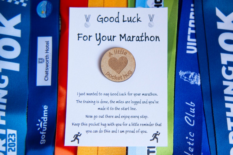 May include: A white card with the text "Good Luck For Your Marathon" and a small wooden token with the text "A little pocket hug".