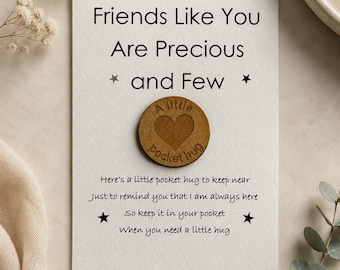 Könnte beinhalten: Eine weiße rechteckige Karte mit dem Text Friends Like You Are Precious and Few und einem kleinen runden Holztoken in der Mitte, der mit einem Herz und den Worten A little pocket hug sowie einem Gedichttext bedruckt ist.