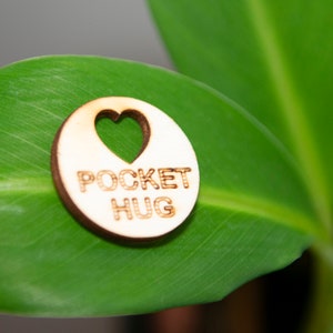 May include: A wooden heart-shaped charm with the text "POCKET HUG" on a green leaf.