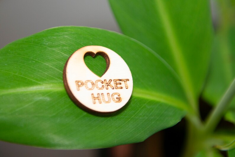 May include: A wooden heart-shaped charm with the text "POCKET HUG" on a green leaf.