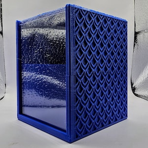 Puede incluir: Una caja azul impresa en 3D con un patrón geométrico en la parte delantera y una ventana de plástico transparente en el lateral.
