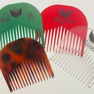 May include: Four beard combs in different colors and materials. The combs are green, brown, red, and clear. Each comb has a beard icon and a name engraved on it. The names are Gabriel, C. Noel, Redy Red, and Mann.