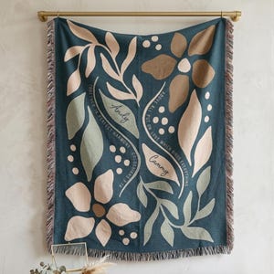 May include: Teal woven throw blanket with floral design and fringe. The blanket features large stylized flowers and leaves in shades of beige, green, and brown. Text includes names "Andy" and "Cammy" and the phrase "Above all put on love which binds everything."