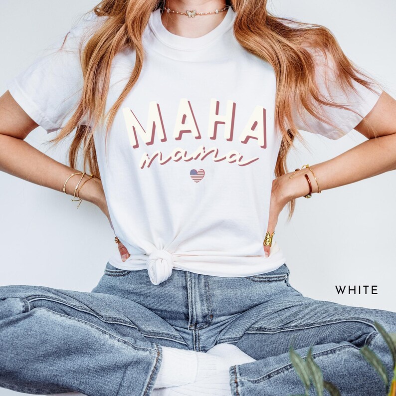 May include: White t-shirt with the text "MAHA" in pink and the text "inspired" in a cursive font with a small American flag heart.