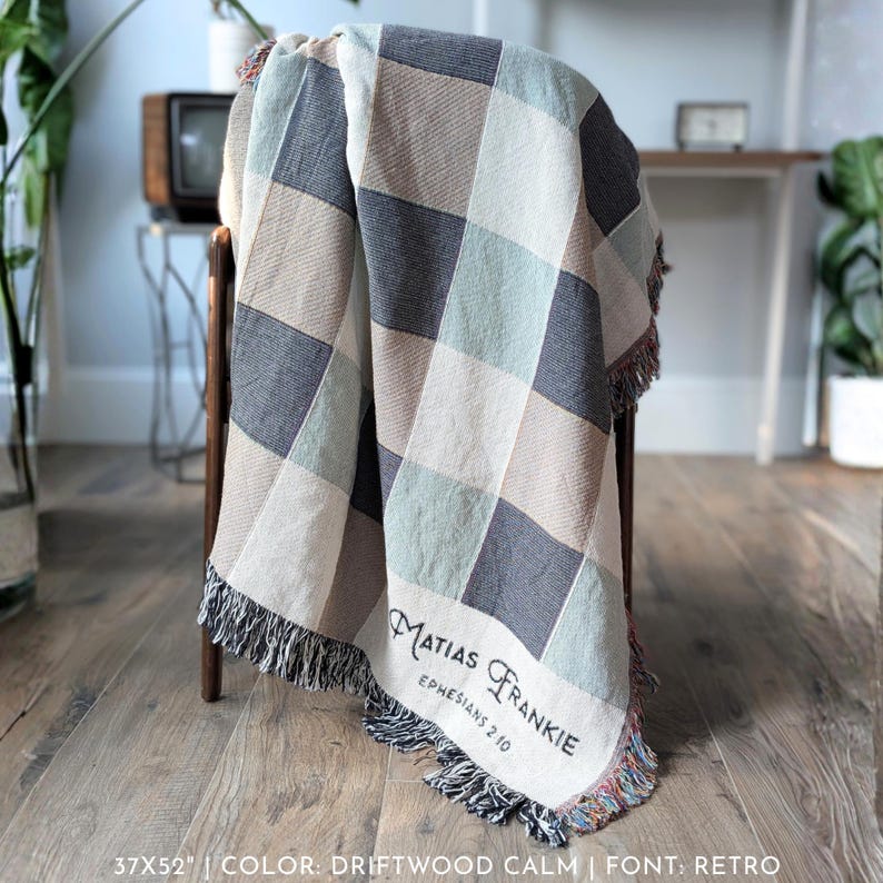 Puede incluir: Una manta tejida con un dise&ntilde;o a cuadros en tonos grises, beige y azul claro, sobre una silla de madera. La manta mide 94x132 cm y tiene un borde con flecos. El texto "MATIAS FRANKIE EPHESIANS 2 10" est&aacute; en la manta.