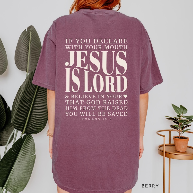 以下が含まれることがあります： 大胆で様式化されたフォントで「JESUS IS LORD」というテキストがプリントされたベリー色のTシャツ。Tシャツの背面には、ローマ人への手紙10:9からの宗教的な引用があります。このシャツは快適なオーバーサイズフィットです。