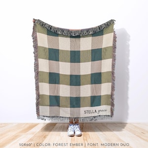 Puede incluir: Una manta tejida con un patr&oacute;n de cuadros en tonos verdes, beige y gris. La manta tiene un borde con flecos y las palabras "stella grace" est&aacute;n escritas en una fuente cursiva. La manta mide 127x152 cm.