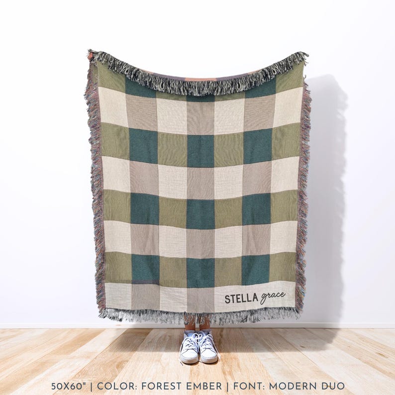 Puede incluir: Una manta tejida con un patr&oacute;n de cuadros en tonos verdes, beige y gris. La manta tiene un borde con flecos y las palabras "stella grace" est&aacute;n escritas en una fuente cursiva. La manta mide 127x152 cm.