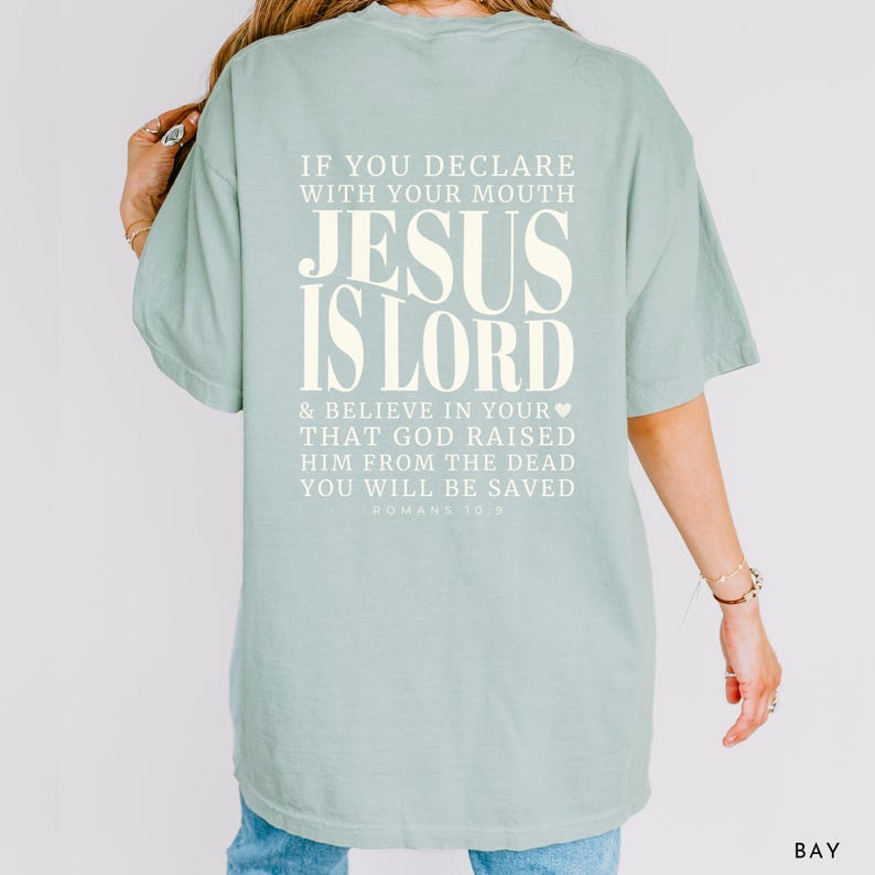 以下が含まれることがあります： 「JESUS IS LORD」の文字が大きくオフホワイトでプリントされた、薄い緑色のTシャツ。背中には「IF YOU DECLARE WITH YOUR MOUTH...YOU WILL BE SAVED」と「ROMANS 10:9」の文字もプリントされています。