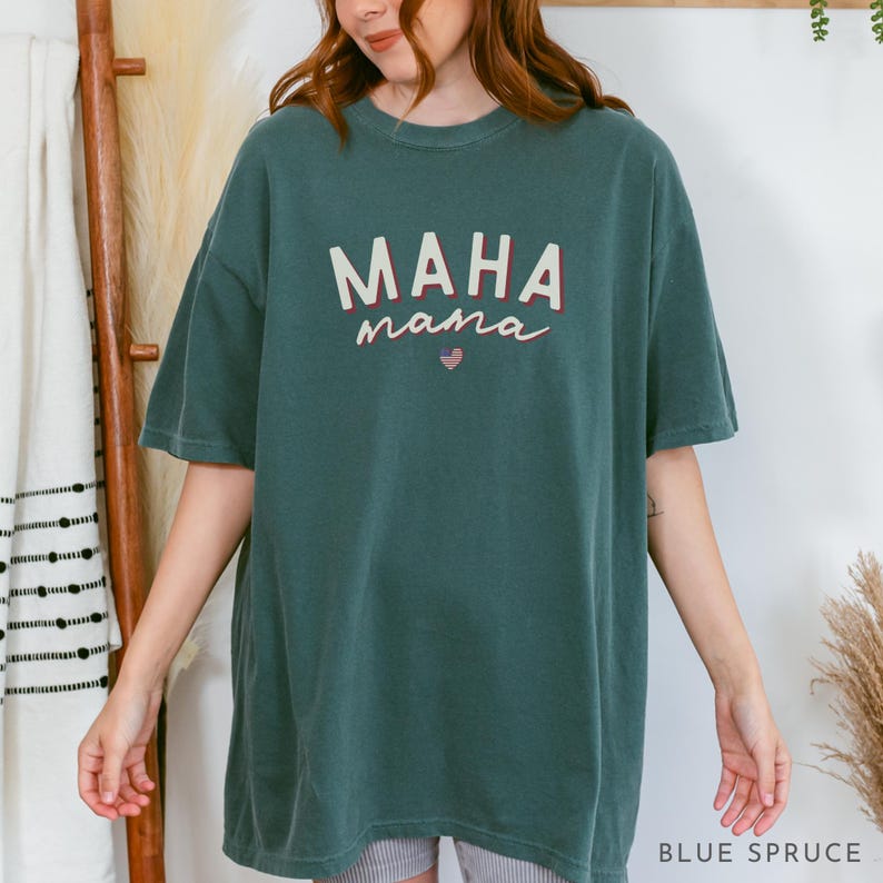 May include: A teal blue oversized t-shirt with the text "MAHA mama" in white and red lettering. A small American flag is inside a red heart.