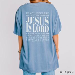 以下が含まれることがあります： 白のテキスト「IF YOU DECLARE WITH YOUR MOUTH JESUS IS LORD & BELIEVE IN YOUR THAT GOD RAISED HIM FROM THE DEAD YOU WILL BE SAVED ROMANS 10:9」がプリントされた、ライトブルーのTシャツ。「BLUE JEAN」とラベルされています。