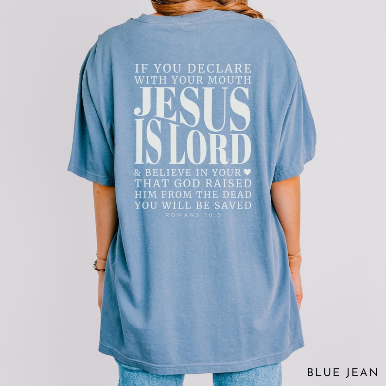 以下が含まれることがあります： 白のテキスト「IF YOU DECLARE WITH YOUR MOUTH JESUS IS LORD & BELIEVE IN YOUR THAT GOD RAISED HIM FROM THE DEAD YOU WILL BE SAVED ROMANS 10:9」がプリントされた、ライトブルーのTシャツ。「BLUE JEAN」とラベルされています。