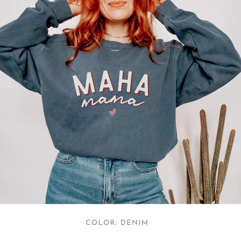 May include: A denim blue sweatshirt with the text "MAHA mama" in white and red lettering. The sweatshirt has a heart with red and white stripes in the center of the text.
