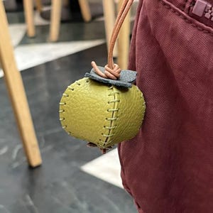 May include: A small, green leather pouch with stitched seams and a brown leather cord. The pouch is attached to a larger, burgundy bag.