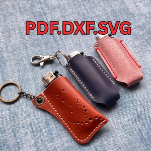 May include: Three leather lighter cases in brown, navy blue, and pink. The brown case has a smiley face design. The navy blue case has white stitching. The pink case has red stitching. The text "PDF.DXF.SVG" is in the background.