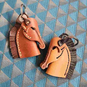 May include: Two leather horse head keychains. One is brown with a brown mane and the other is brown with a black mane.