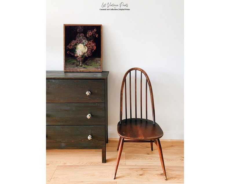 May include: A dark wood dresser with three drawers and a framed print of a floral still life above it. A dark wood chair with a curved back and spindle design sits to the right of the dresser. The chair and dresser are in front of a white wall.