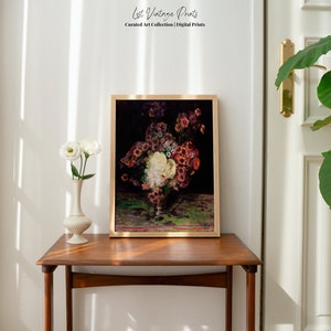 May include: A framed vintage art print of a still life featuring a bouquet of red, white, and pink flowers in a vase on a green tablecloth. The print is displayed on a wooden table in a room with white walls.