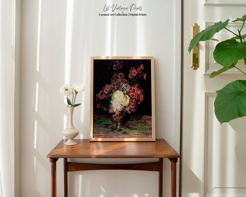 May include: A framed vintage art print of a still life featuring a bouquet of red, white, and pink flowers in a vase on a green tablecloth. The print is displayed on a wooden table in a room with white walls.