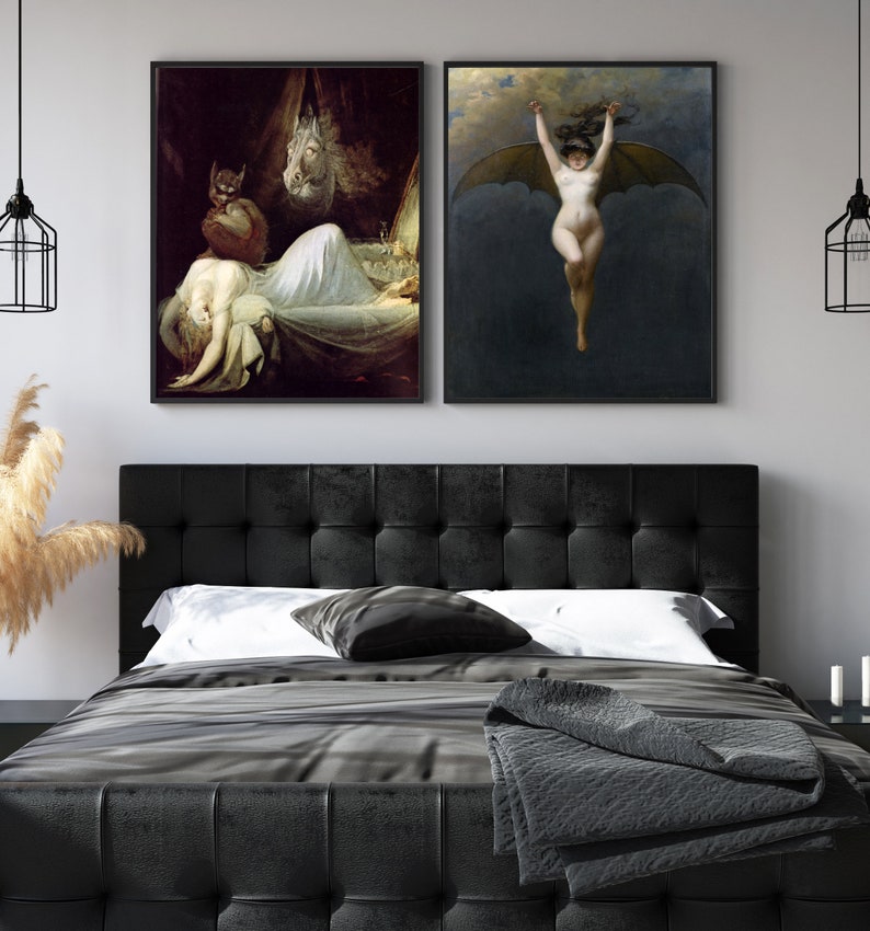 May include: Two framed black and white art prints depicting a woman with bat wings and a woman sleeping in a bed with a demon figure. The prints are hanging on a white wall above a black tufted headboard.