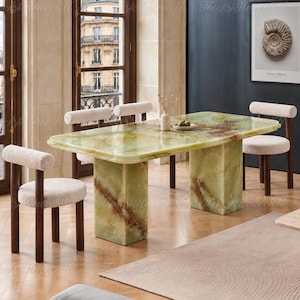 May include: A rectangular dining table with a polished light green onyx surface featuring brown veining, supported by two matching block pedestals. Four chairs with dark wood frames and cream-colored textured fabric seats and backrests.