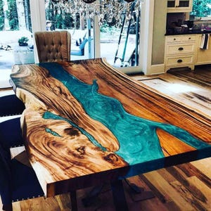 Op de afbeelding: Een handgemaakte houten eettafel met een turquoise epoxyhars rivierontwerp. De tafel heeft een natuurlijke houtnerf afwerking en is ongeveer 244 cm lang en 102 cm breed. De tafel wordt ondersteund door donkere metalen poten.