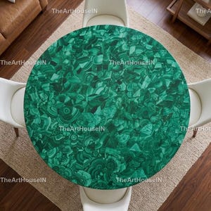 Op de afbeelding: Bovenaanzicht van een ronde tafel met een levendig groen malachiet oppervlak. De tafel wordt omringd door vier witte stoelen, geplaatst op een neutraal gekleurd tapijt. Het malachietpatroon heeft wervelende groentinten.