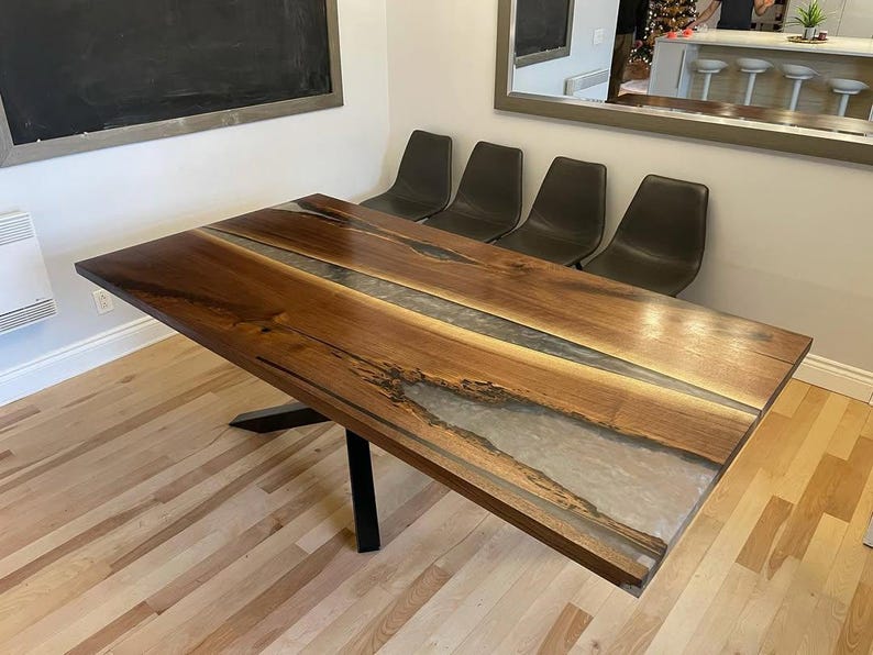 May include: A rectangular wooden dining table with a dark walnut finish and a clear epoxy river running through the center. The table is supported by a black metal base. The table measures approximately 72 inches long.