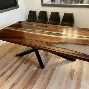 May include: A rectangular wooden dining table with a dark brown finish and a clear epoxy river down the center. The table is supported by a black metal base. The table measures approximately 72 inches long.