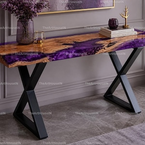 May include: A modern console table with a wooden top and purple resin accents. The table has black metal X-shaped legs. A vase of purple flowers, books, and decorative items are on the table.
