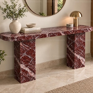 Può includere: Un tavolo console rettangolare con bordi arrotondati, realizzato in marmo rosso intenso con venature bianche prominenti. Il tavolo presenta due gambe spesse a forma di blocco e una superficie liscia e lucida, offrendo un mobile robusto ed elegante.
