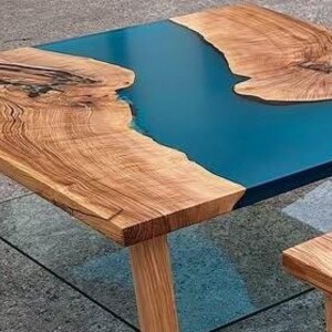 May include: A handcrafted wooden coffee table with a striking blue epoxy resin river design. The table features natural wood grain and a rectangular shape, supported by four wooden legs. The table's dimensions are approximately 36 inches long, 24 inches wide, and 18 inches high.