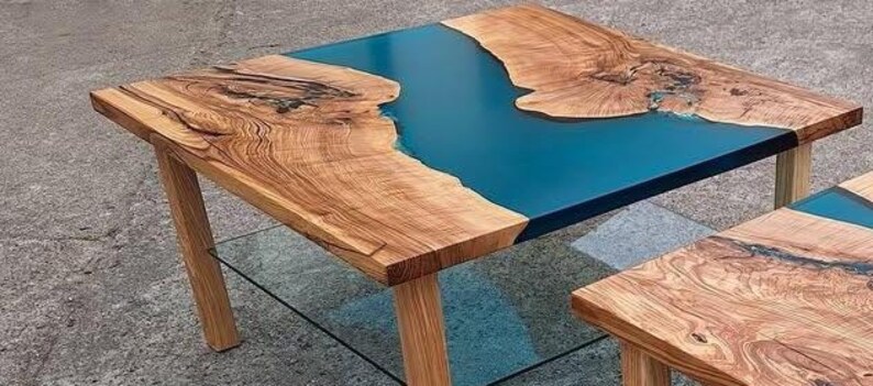 May include: A handcrafted wooden coffee table with a striking blue epoxy resin river design. The table features natural wood grain and a rectangular shape, supported by four wooden legs. The table's dimensions are approximately 36 inches long, 24 inches wide, and 18 inches high.
