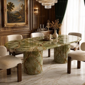 Puede incluir: Una mesa de comedor ovalada con superficie de ónix verde pulido y dos bases cilíndricas estriadas, rodeada por cuatro sillas con tapicería texturizada color crema y marcos de madera oscura en un entorno interior formal.