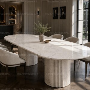 May include: An oval dining table with a polished white marble top and two cylindrical, fluted stone bases. The table is surrounded by six upholstered chairs with curved backrests and dark wooden legs, featuring a light beige fabric finish.