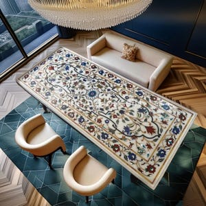 Puede incluir: Una mesa rectangular de mármol blanco con intrincados incrustaciones florales en rojo, azul y verde. La mesa está rodeada por dos sillas color crema y un sofá beige. Una gran lámpara de araña cuelga sobre la mesa, y el suelo es una mezcla de madera y baldosas estampadas.